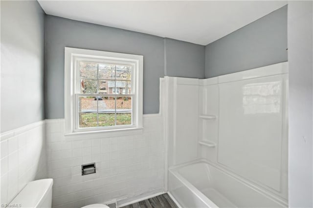 bathroom featuring washtub / shower combination, wood-type flooring, toilet, and tile walls