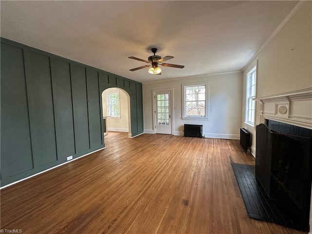 living area with arched walkways, radiator, a fireplace, and wood finished floors