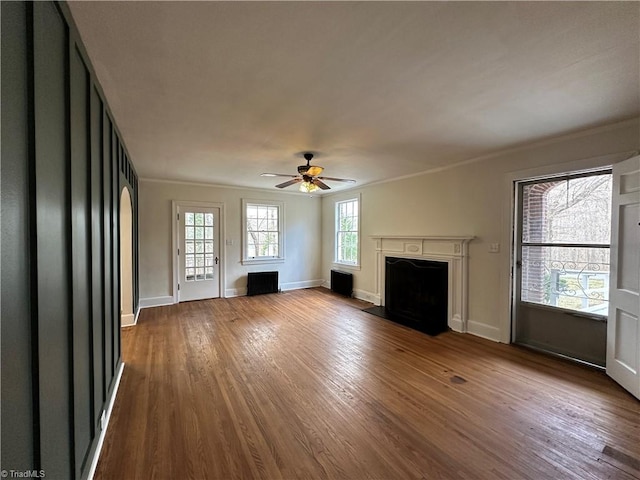 unfurnished living room featuring a fireplace with flush hearth, a ceiling fan, ornamental molding, wood finished floors, and baseboards