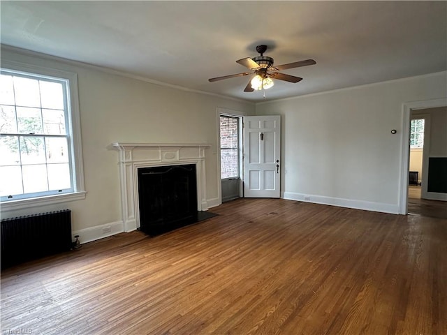 unfurnished living room with radiator, a premium fireplace, wood finished floors, crown molding, and a healthy amount of sunlight