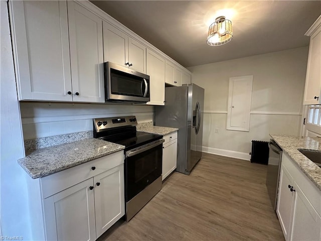 kitchen with stainless steel appliances, light stone counters, wood finished floors, and white cabinetry