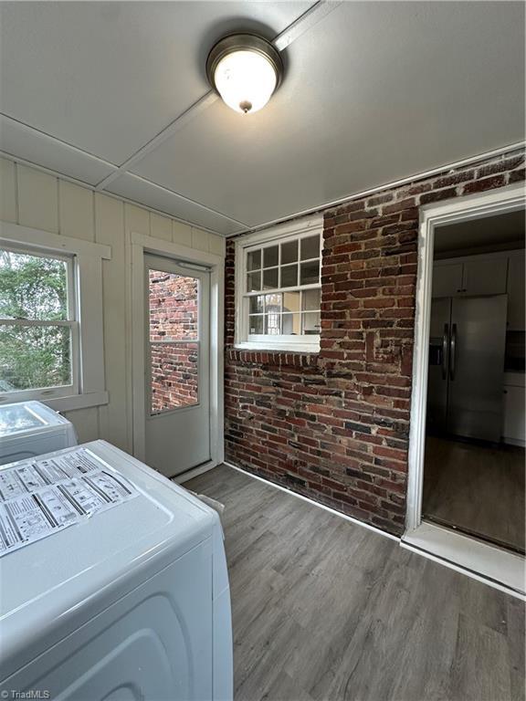 laundry room featuring washing machine and dryer, laundry area, brick wall, and wood finished floors