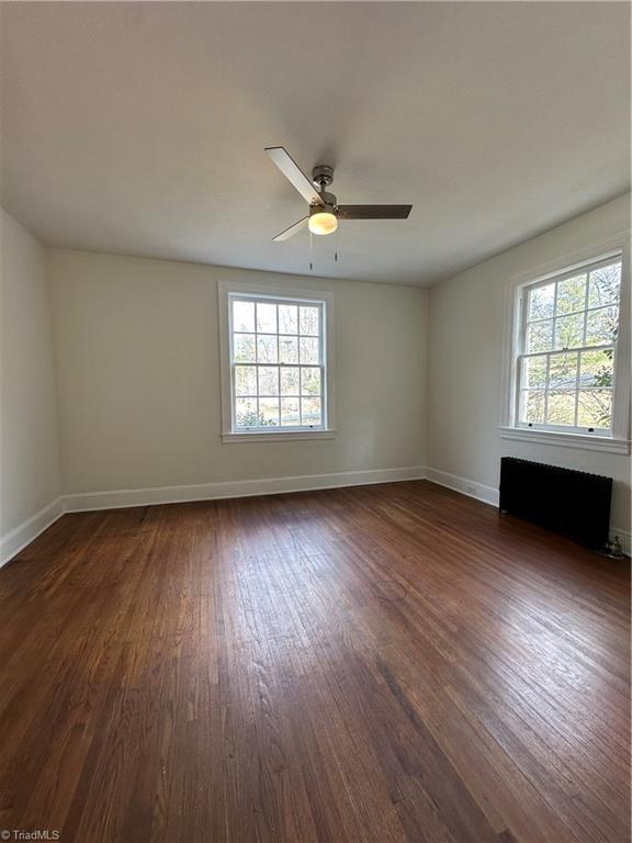 unfurnished room with dark wood-style floors, radiator heating unit, baseboards, and a ceiling fan