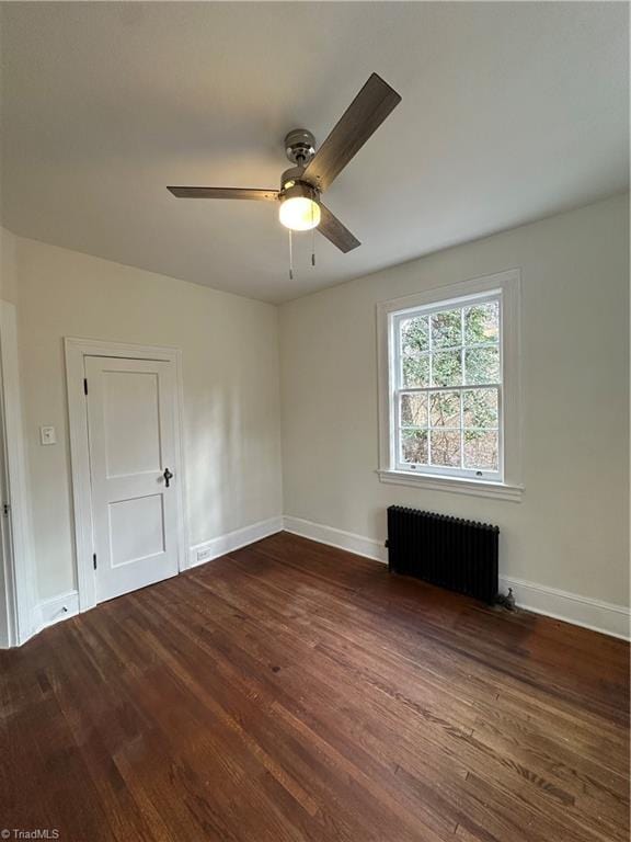 empty room featuring baseboards, ceiling fan, dark wood-type flooring, and radiator