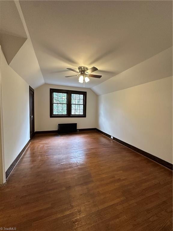 additional living space featuring dark wood finished floors, lofted ceiling, radiator heating unit, ceiling fan, and baseboards