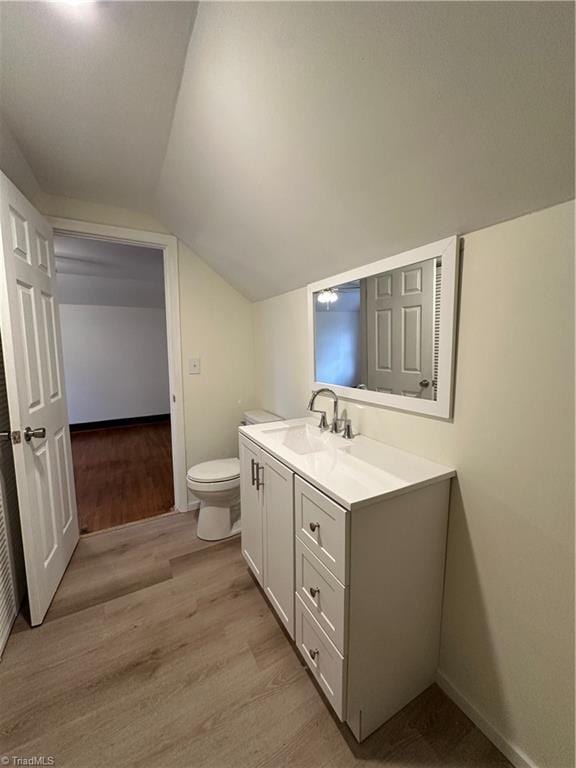 bathroom with lofted ceiling, toilet, vanity, wood finished floors, and baseboards