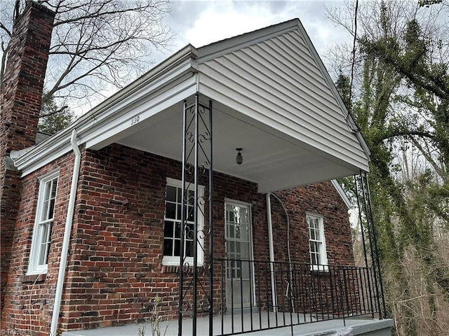 view of property exterior featuring a porch, brick siding, and a chimney