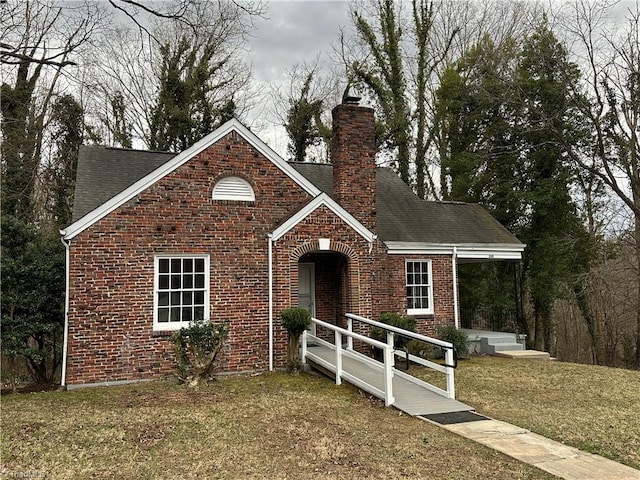 view of front of house with a shingled roof, brick siding, a chimney, and a front lawn