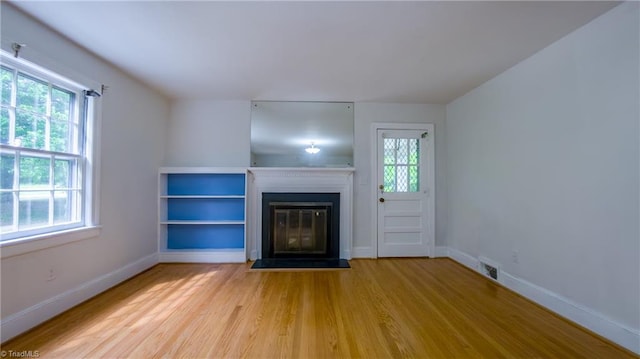 unfurnished living room featuring wood finished floors, a glass covered fireplace, and baseboards