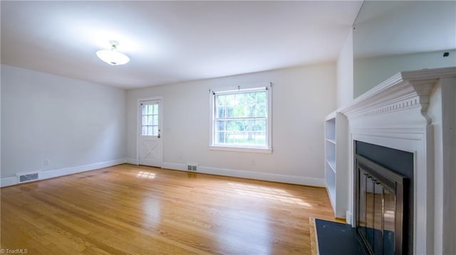 unfurnished living room featuring light wood finished floors, baseboards, and a fireplace with flush hearth