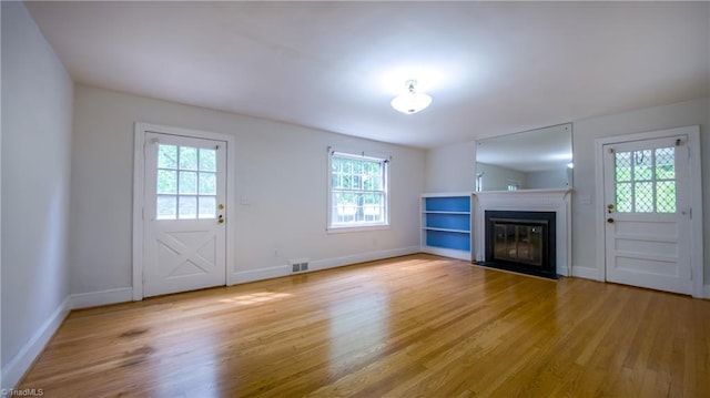 unfurnished living room with light wood-style floors, baseboards, and a fireplace with flush hearth