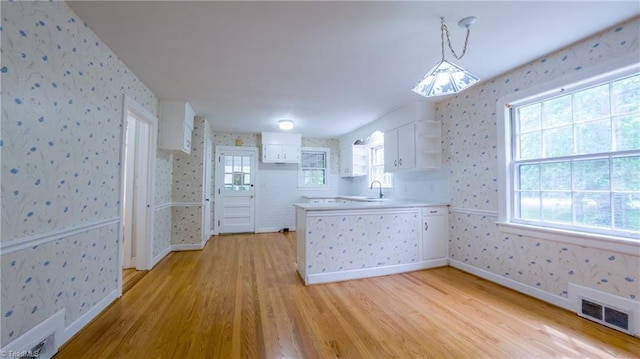kitchen with wallpapered walls, light wood finished floors, a peninsula, open shelves, and white cabinetry