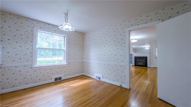 unfurnished dining area featuring wallpapered walls, light wood-type flooring, baseboards, and a glass covered fireplace