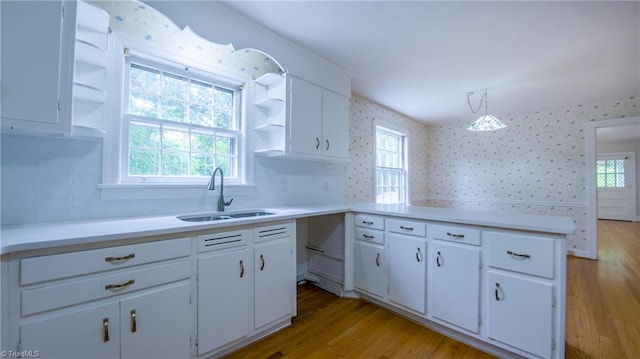 kitchen featuring a sink, wallpapered walls, light wood finished floors, white cabinetry, and light countertops