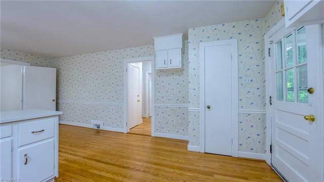 unfurnished bedroom with light wood finished floors, wallpapered walls, and baseboards