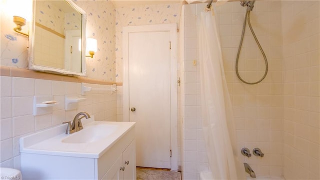 full bathroom with wallpapered walls, shower / bathtub combination with curtain, vanity, and a wainscoted wall