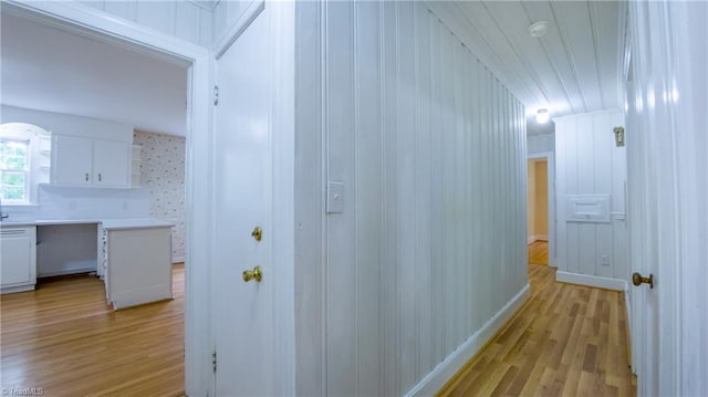 hall featuring light wood-type flooring, baseboards, and arched walkways
