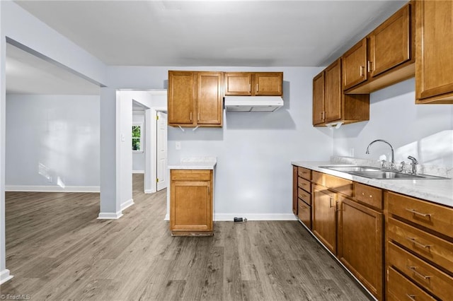 kitchen featuring a sink, under cabinet range hood, dark wood-style flooring, and brown cabinetry