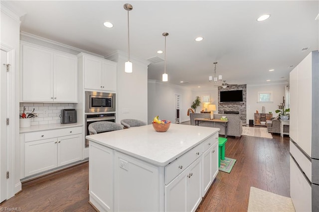 kitchen featuring white cabinetry, stainless steel appliances, decorative light fixtures, and a kitchen island