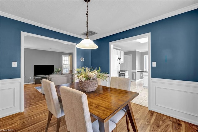 dining space featuring visible vents, ornamental molding, light wood-type flooring, and a wainscoted wall