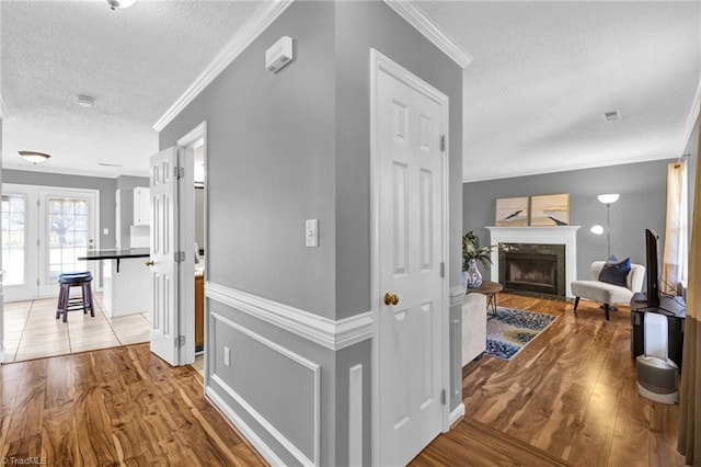 corridor featuring light wood finished floors, visible vents, a textured ceiling, and crown molding