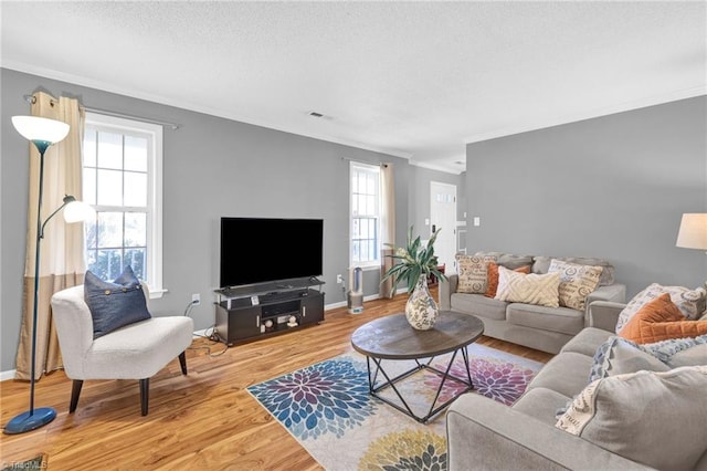 living area with visible vents, a textured ceiling, wood finished floors, and ornamental molding