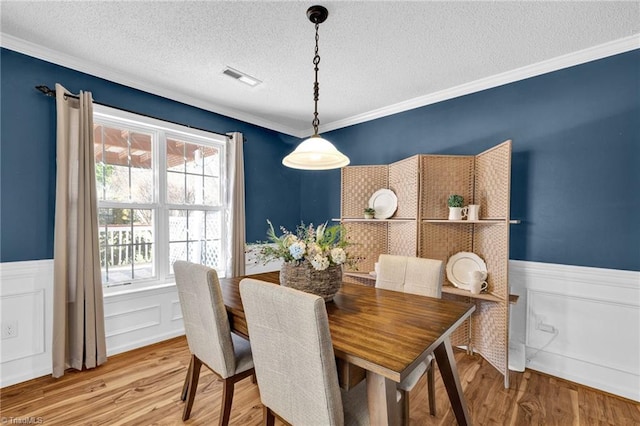 dining area featuring visible vents, a textured ceiling, wood finished floors, wainscoting, and crown molding