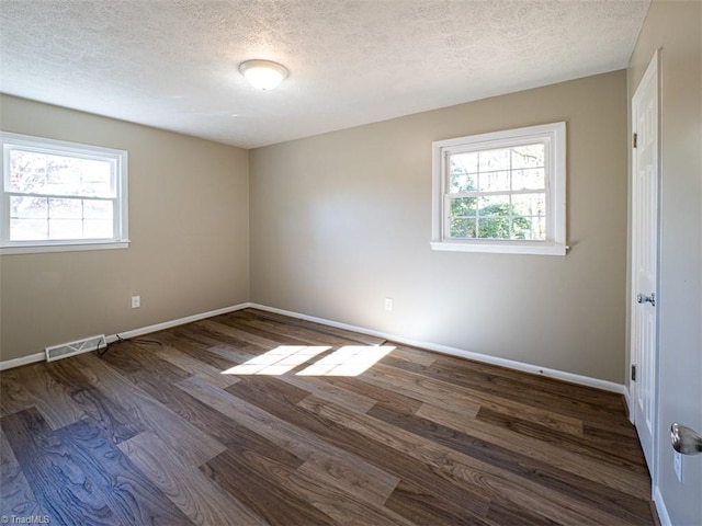 empty room featuring dark hardwood / wood-style floors, a healthy amount of sunlight, and a textured ceiling