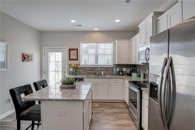 1438 Crestlawn Trl, Pfafftown, NC 27040 - kitchen with appliances with stainless steel finishes, a sink, a breakfast bar area, backsplash, and light wood-type flooring