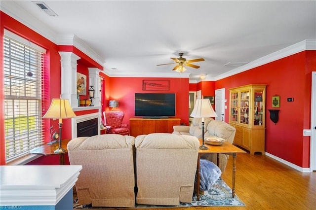 living room with wood finished floors, a ceiling fan, crown molding, baseboards, and a glass covered fireplace
