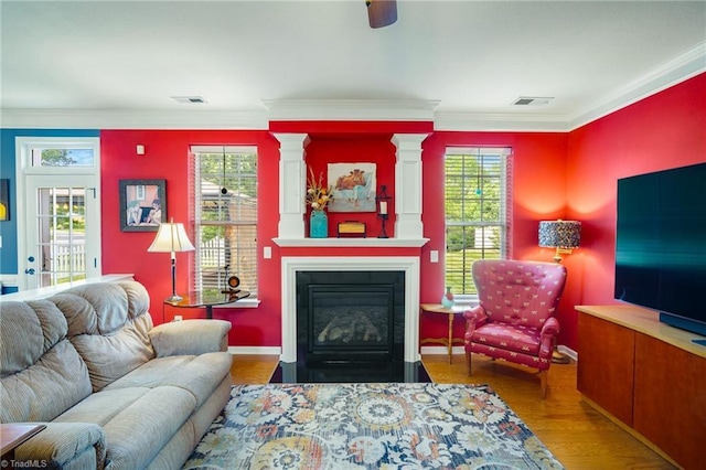 living room featuring a large fireplace, decorative columns, ornamental molding, and wood finished floors