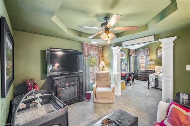 living room with ornate columns, carpet, ceiling fan, a raised ceiling, and a glass covered fireplace