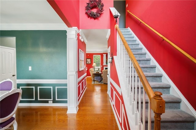staircase featuring wood finished floors, ornate columns, and ornamental molding