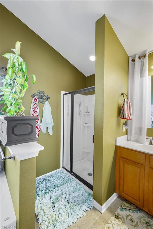 full bath with a shower stall, vaulted ceiling, tile patterned floors, vanity, and baseboards