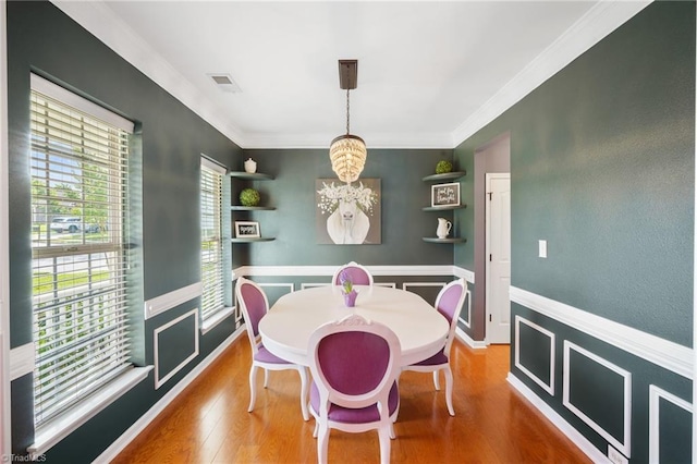 dining area featuring a chandelier, ornamental molding, wood finished floors, and a wainscoted wall