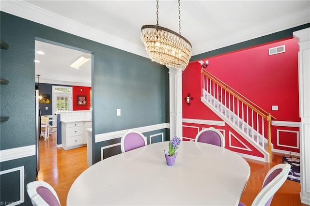 dining room featuring decorative columns, wood finished floors, a chandelier, stairs, and ornamental molding