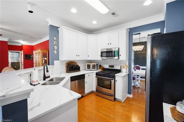 kitchen with appliances with stainless steel finishes, a sink, a peninsula, light wood-type flooring, and tasteful backsplash