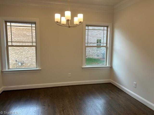 unfurnished dining area featuring a notable chandelier, baseboards, ornamental molding, and dark wood-style floors