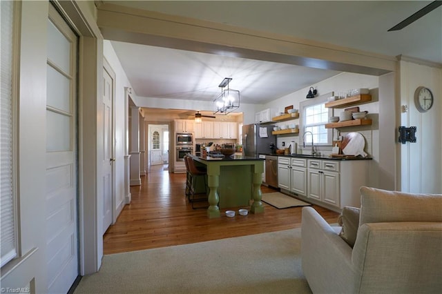 kitchen featuring open shelves, a sink, dark countertops, a center island, and stainless steel appliances