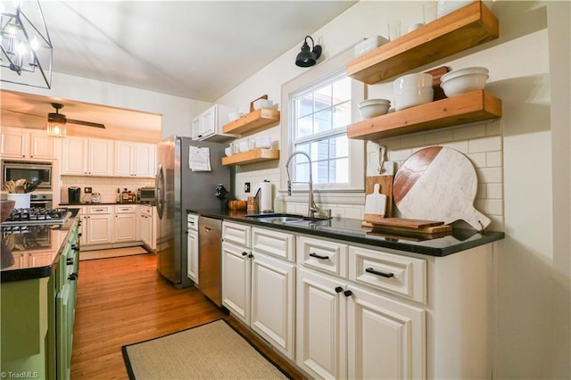 kitchen with open shelves, dark countertops, appliances with stainless steel finishes, and a sink