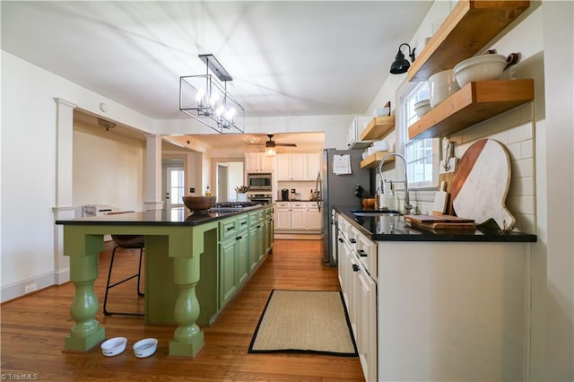 kitchen with dark countertops, a sink, green cabinets, stainless steel appliances, and open shelves