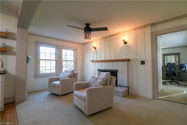 sitting room featuring crown molding, ceiling fan, carpet floors, a fireplace, and a decorative wall