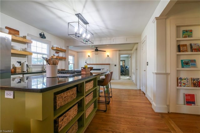 kitchen with green cabinetry, open shelves, light wood-style floors, dark countertops, and backsplash