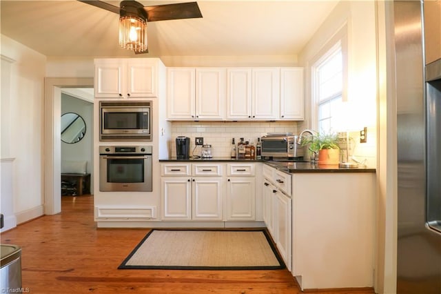 kitchen featuring dark countertops, tasteful backsplash, light wood-type flooring, appliances with stainless steel finishes, and white cabinetry