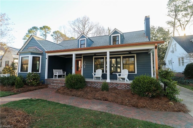 view of front of property featuring covered porch, a chimney, and roof with shingles