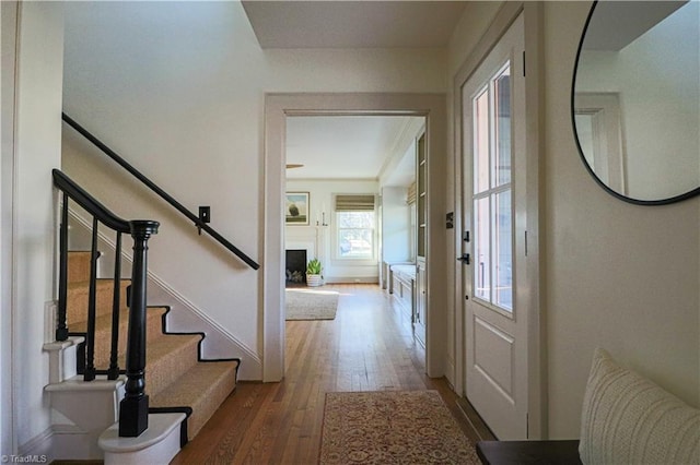 foyer with hardwood / wood-style flooring, stairway, a fireplace with raised hearth, and baseboards