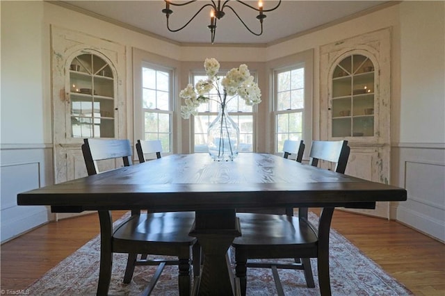 dining room with ornamental molding, wood finished floors, wainscoting, a decorative wall, and a chandelier