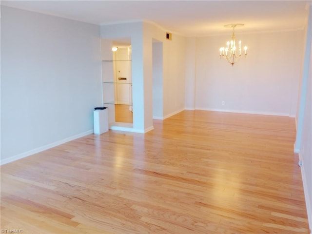 spare room featuring a chandelier and light hardwood / wood-style floors