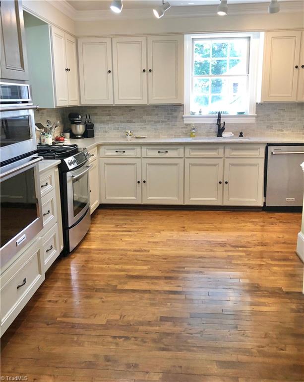 kitchen featuring white cabinets, sink, backsplash, appliances with stainless steel finishes, and light wood-type flooring