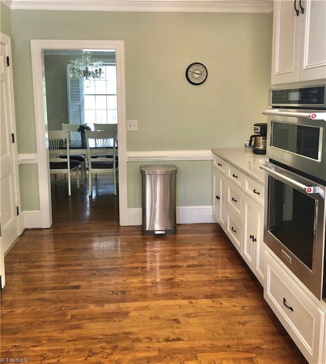 kitchen featuring dark wood-type flooring, white cabinets, stainless steel double oven, an inviting chandelier, and crown molding